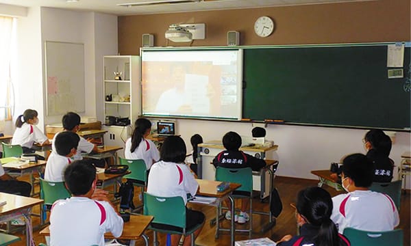 オンラインで交流する様子を教室の生徒全員で視聴している場面